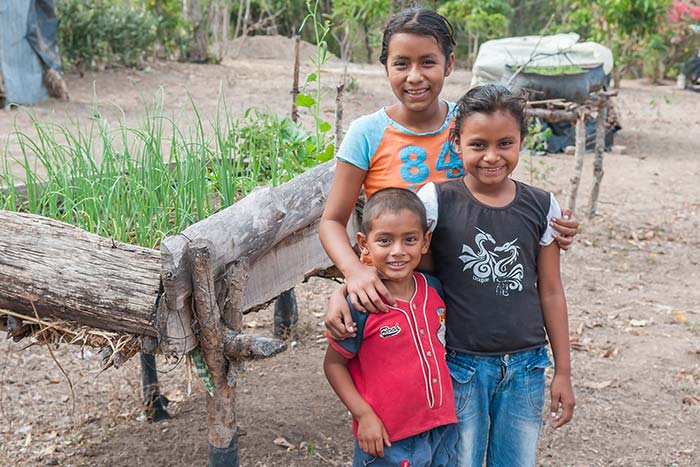 Three smiling children in rural Nicaragua with their arms around each other.
